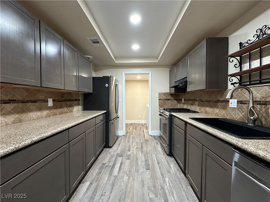 117 Boysenberry Lane Henderson, NV 89074 - Photo 12 of 22 Kitchen featuring decorative backsplash, appliances with stainless steel finishes, light stone counters, and a tray ceiling