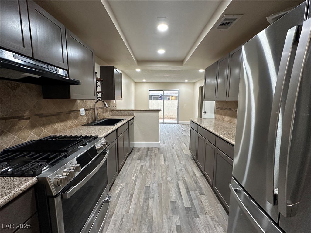 117 Boysenberry Lane Henderson, NV 89074 - Photo 13 of 22 Kitchen with stainless steel appliances, a raised ceiling, light stone countertops, light wood-style flooring, and under cabinet range hood