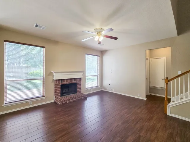 an empty room with wooden floor fireplace and windows