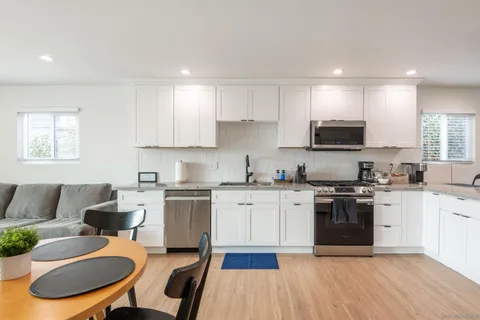 a kitchen with stainless steel appliances granite countertop a stove top oven a sink dishwasher and white cabinets with wooden floor