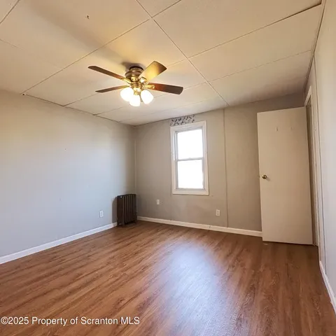 an empty room with wooden floor fan and windows
