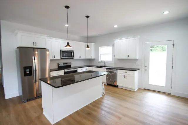 a kitchen with stainless steel appliances granite countertop a sink a stove a refrigerator and island with wooden floor