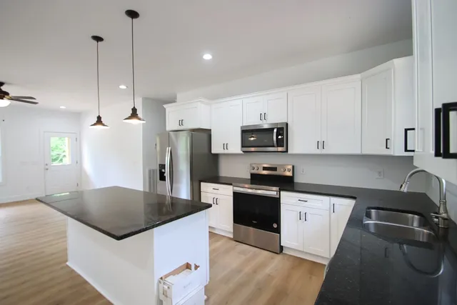 a kitchen with stainless steel appliances granite countertop a sink a stove a refrigerator and island with wooden floor