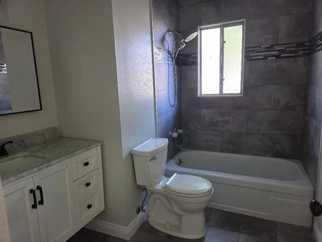 a bathroom with a granite countertop bathtub shower sink vanity and toilet