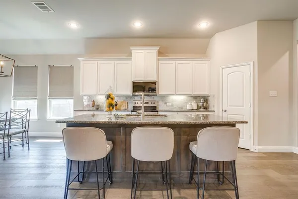 a kitchen with stainless steel appliances granite countertop a sink a stove top oven a refrigerator with wooden cabinets and floor