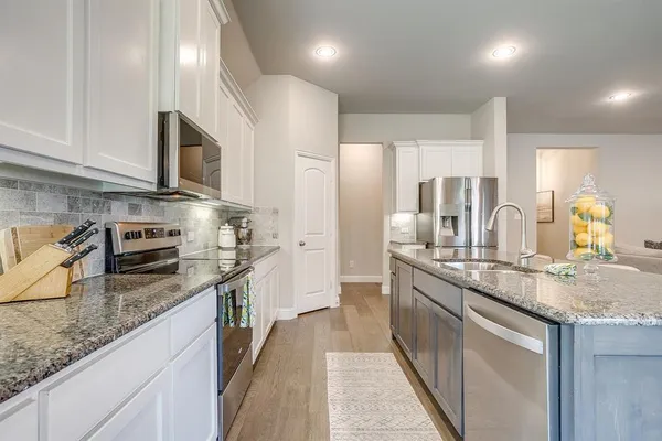 a kitchen with stainless steel appliances kitchen island granite countertop a table chairs stove and white cabinets