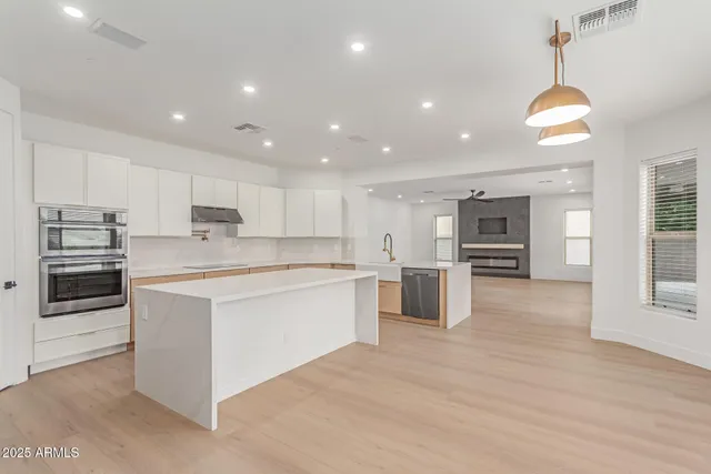 a large kitchen with stainless steel appliances kitchen island granite countertop a stove a sink a refrigerator and white cabinets with wooden floor