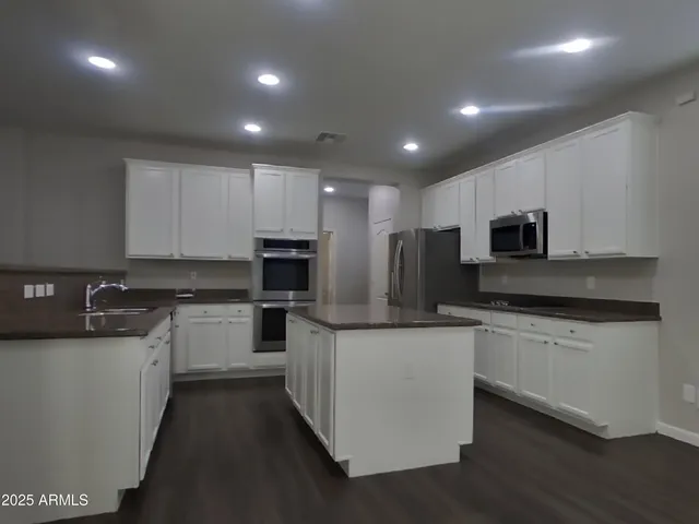 a kitchen with stainless steel appliances a sink dishwasher a stove top oven a refrigerator with white cabinets and wooden floor