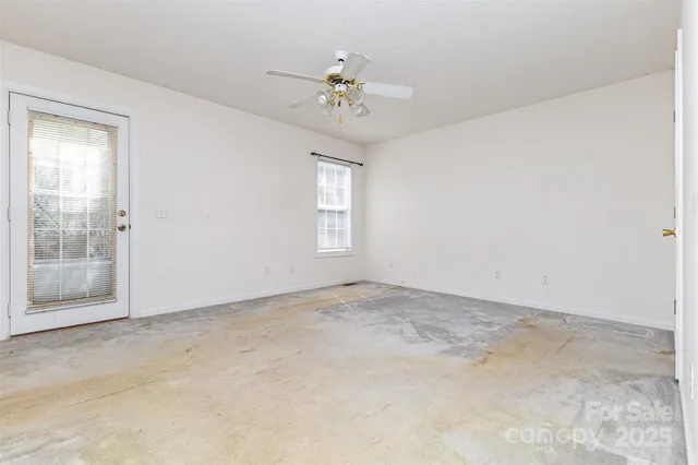 an empty room with a chandelier fan and windows