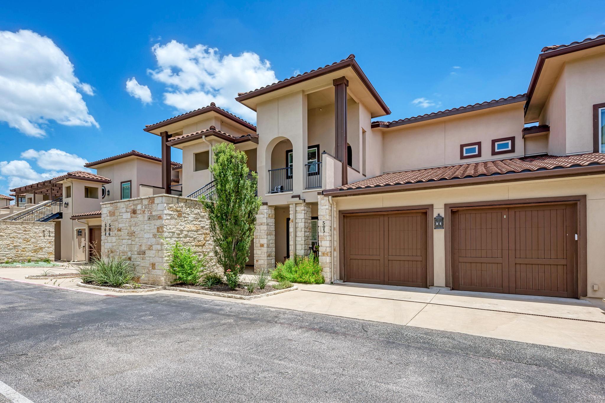 2601 North Quinlan Park Road, Unit 506 Austin, TX 78732 - Photo 2 of 39 A terracotta-tiled roof crowns this stucco residence, featuring a stone accent wall and two prominent garage doors.