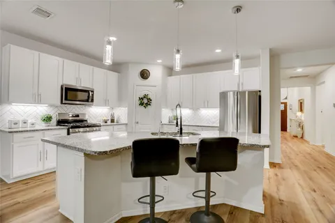 a kitchen with stainless steel appliances granite countertop a refrigerator a stove a sink cabinets and a dining table with wooden floor