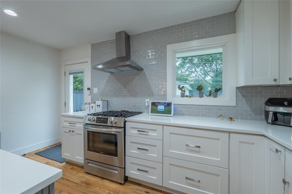 864 Peavy Road Dallas, TX 75218 - Photo 8 of 21 Kitchen featuring white shaker cabinetry, stainless steel range with overhead hood, quartz countertops, and a gray subway tile backsplash