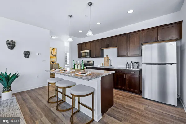 a kitchen with stainless steel appliances granite countertop a refrigerator a stove a sink dishwasher and a dining table with wooden floor