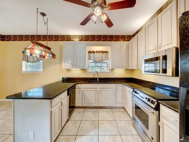 a view of an empty room with chandelier fan and kitchen view