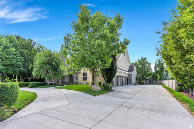 650 East Center Street Alpine, UT 84004 - Photo 3 of 38 Expansive concrete driveway with a circular drive, lush green landscaping, mature trees, and a multi-car garage