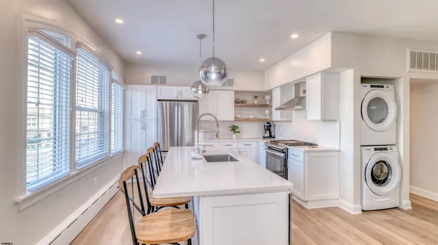 a kitchen with stainless steel appliances granite countertop a sink a stove a washer dryer and white cabinets next to a window