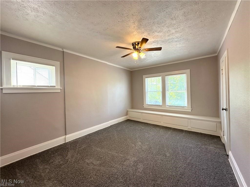 3277 Cedarbrook Road Cleveland, OH 44118 - Photo 9 of 18 Unfurnished room with dark carpet, a textured ceiling, ornamental molding, and ceiling fan