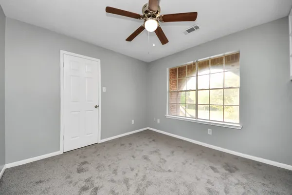 an empty room with chandelier fan and windows