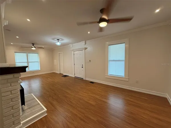 an empty room with wooden floor a ceiling fan and windows