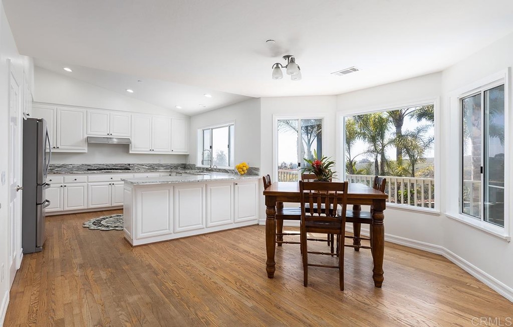 6949 Elfin Oaks Road Escondido, CA 92029 - Photo 7 of 24 a kitchen with a table chairs wooden floors and white stainless steel appliances