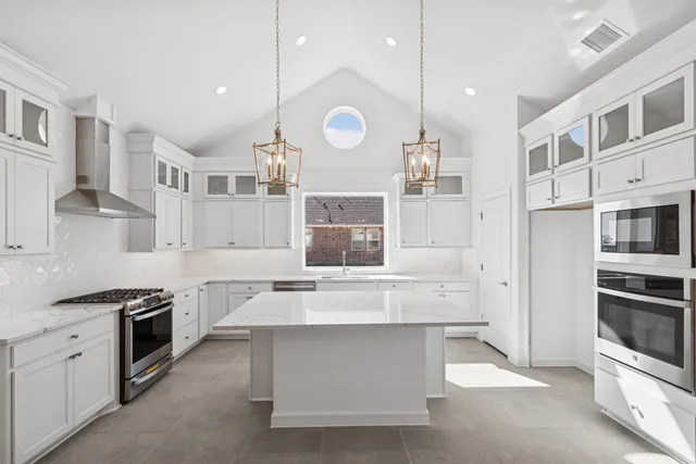 a large kitchen with stainless steel appliances a stove a sink and a white cabinets