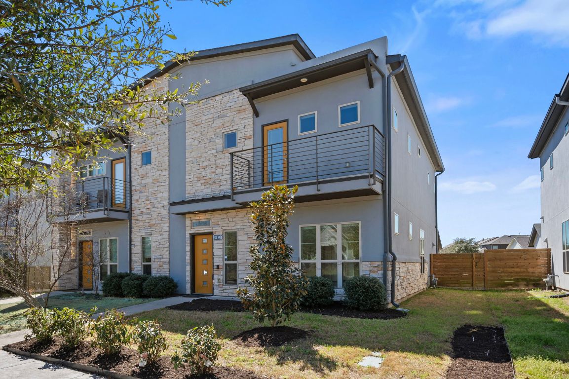 View of front of property featuring stucco siding, a front lawn, stone siding, fence, and a balcony