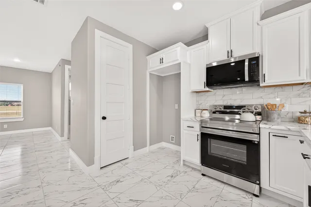 a large white kitchen with a large counter top space a sink stainless steel appliances and cabinets