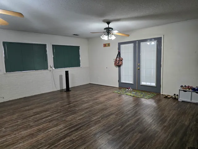 a view of an empty room with wooden floor and fan