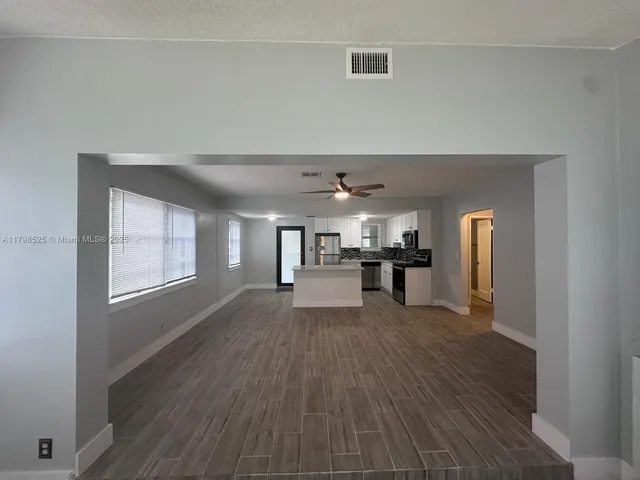 a view of empty room with wooden floor and kitchen view