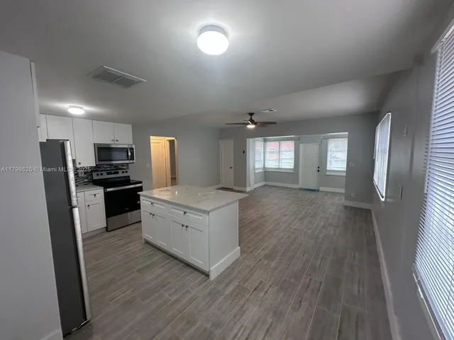 a kitchen with stainless steel appliances granite countertop a stove a sink dishwasher a refrigerator and white cabinets with wooden floor