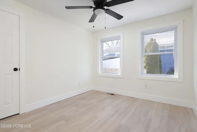 an empty room with wooden floor ceiling fan and windows
