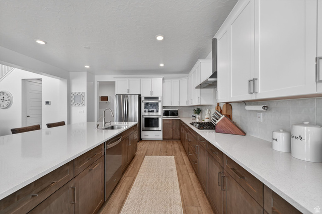 1165 West Union Bench Drive Mapleton, UT 84664 - Photo 16 of 61 Contemporary kitchen featuring a large island with sink, stainless steel appliances, two-tone cabinetry, light-colored countertops, and wood-finish flooring