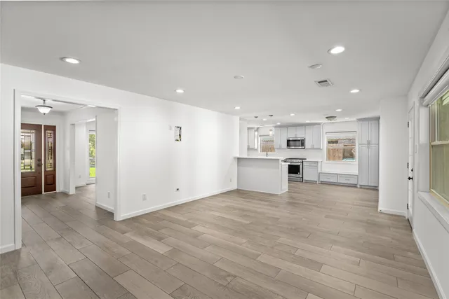 a view of an empty room with wooden floor and a kitchen