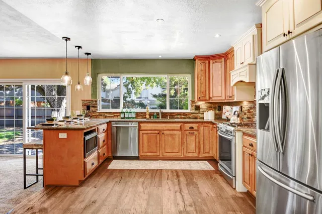 a kitchen with stainless steel appliances granite countertop a stove a refrigerator a sink and dishwasher with wooden floor