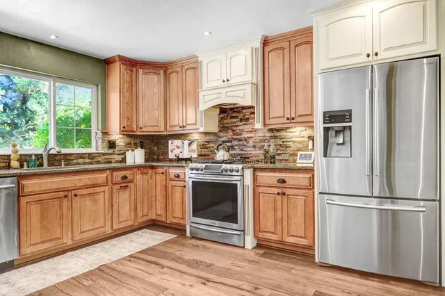 a kitchen with stainless steel appliances granite countertop a refrigerator oven a sink dishwasher and white cabinets with wooden floor