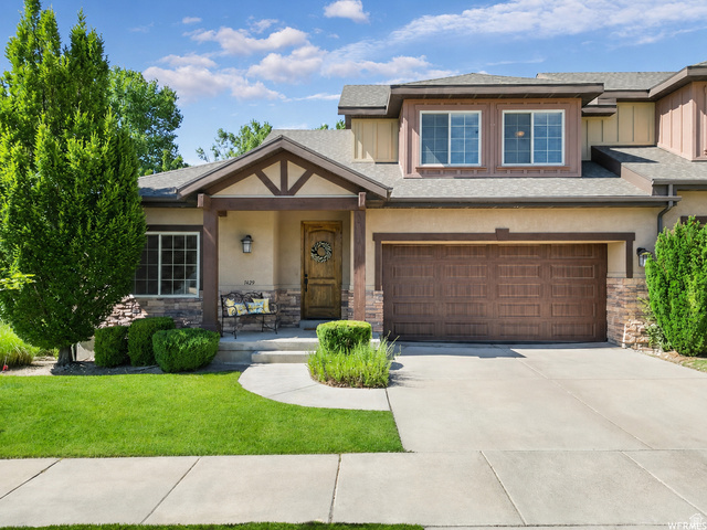 1429 Chateau Ridge Way Sandy, UT 84092 - Photo 20 of 22 Exterior featuring a covered entryway, decorative stone accents, a wood-finish front door, a two-car garage with a brown door, and a manicured lawn