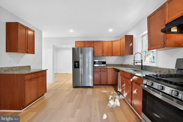 a kitchen with stainless steel appliances granite countertop a stove a sink dishwasher a refrigerator and wooden cabinets with wooden floor