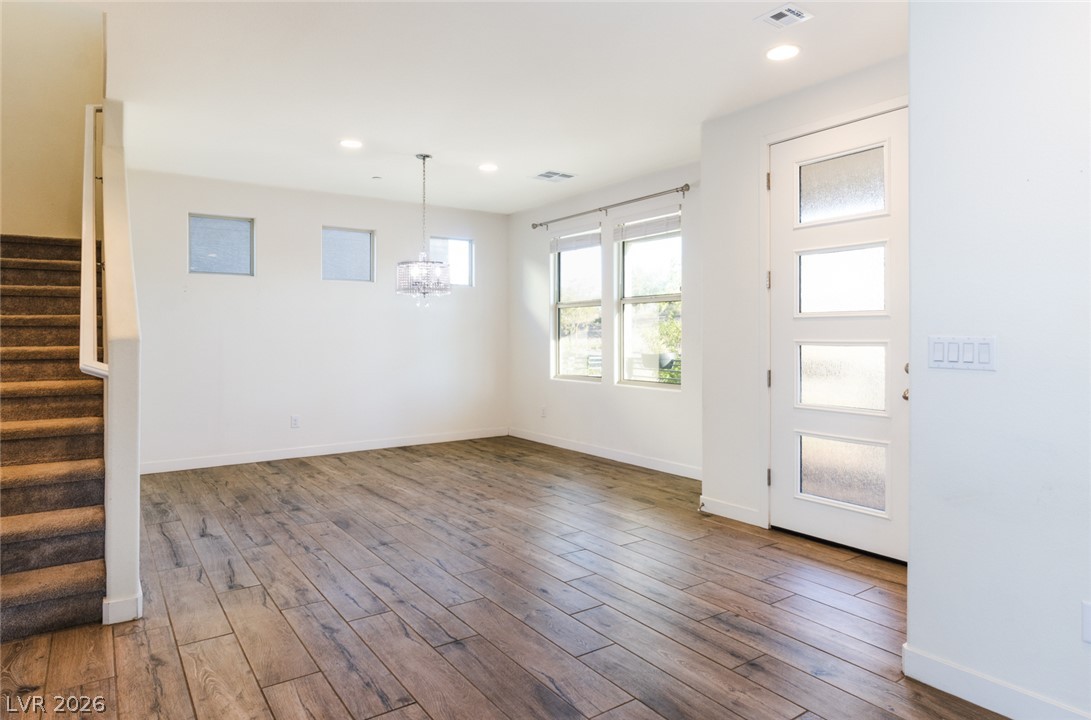920 East Sunset Road Henderson, NV 89011 - Photo 7 of 33 Sun-filled living area featuring warm wood flooring, a decorative chandelier, and abundant natural light from large windows and a glass-paneled entry door.