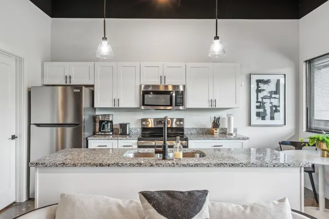 a kitchen with granite countertop a refrigerator a stove a sink and white cabinets