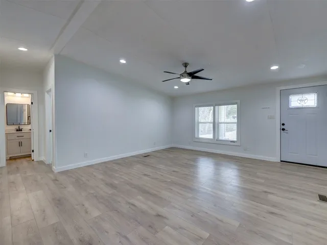 an empty room with wooden floor a ceiling fan and kitchen view