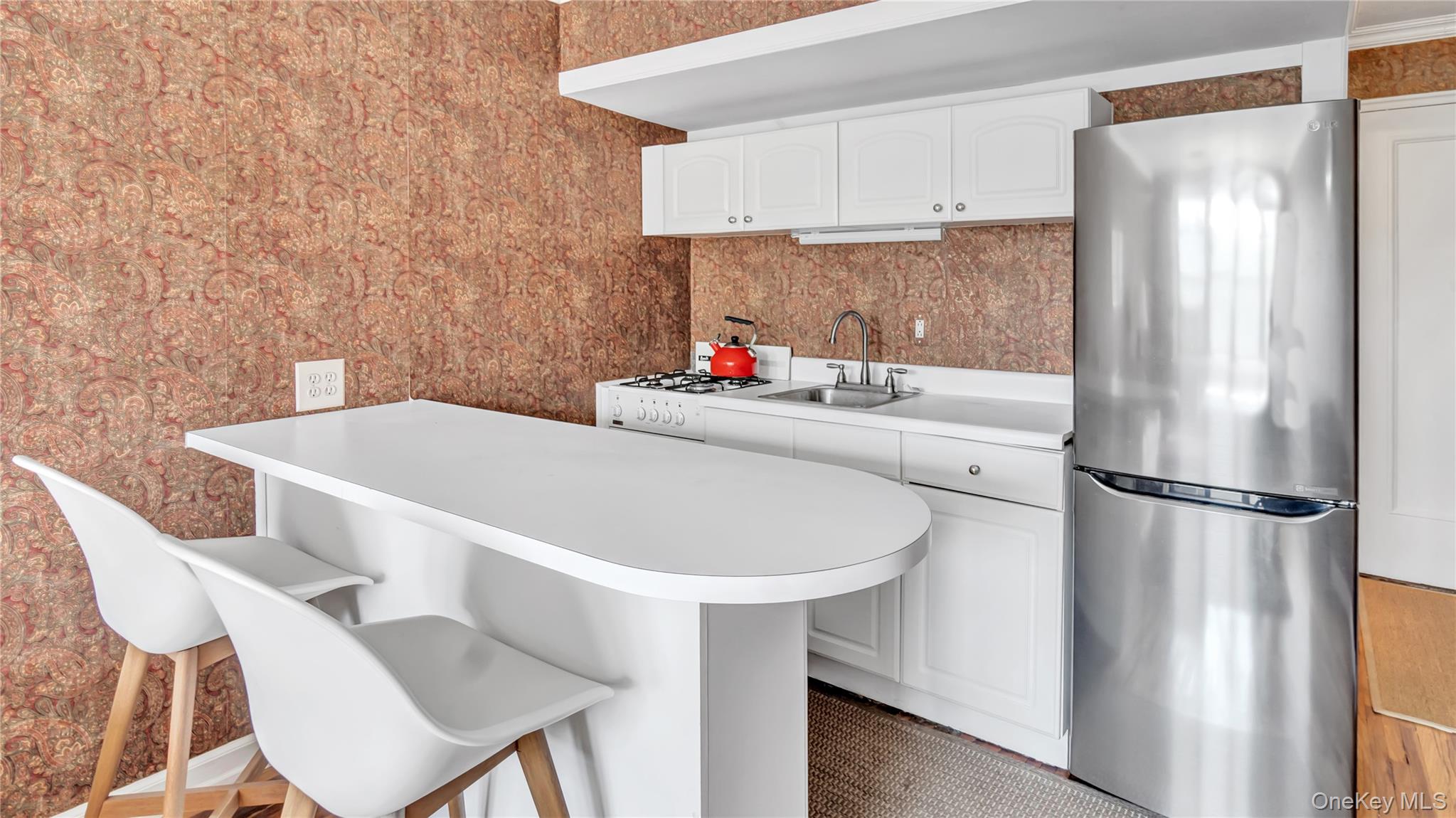 15 Canterbury Road, Unit D18 Great Neck, NY 11021 - Photo 5 of 10 Kitchen with freestanding refrigerator, white cabinets, a kitchen bar, light countertops, and white gas range oven