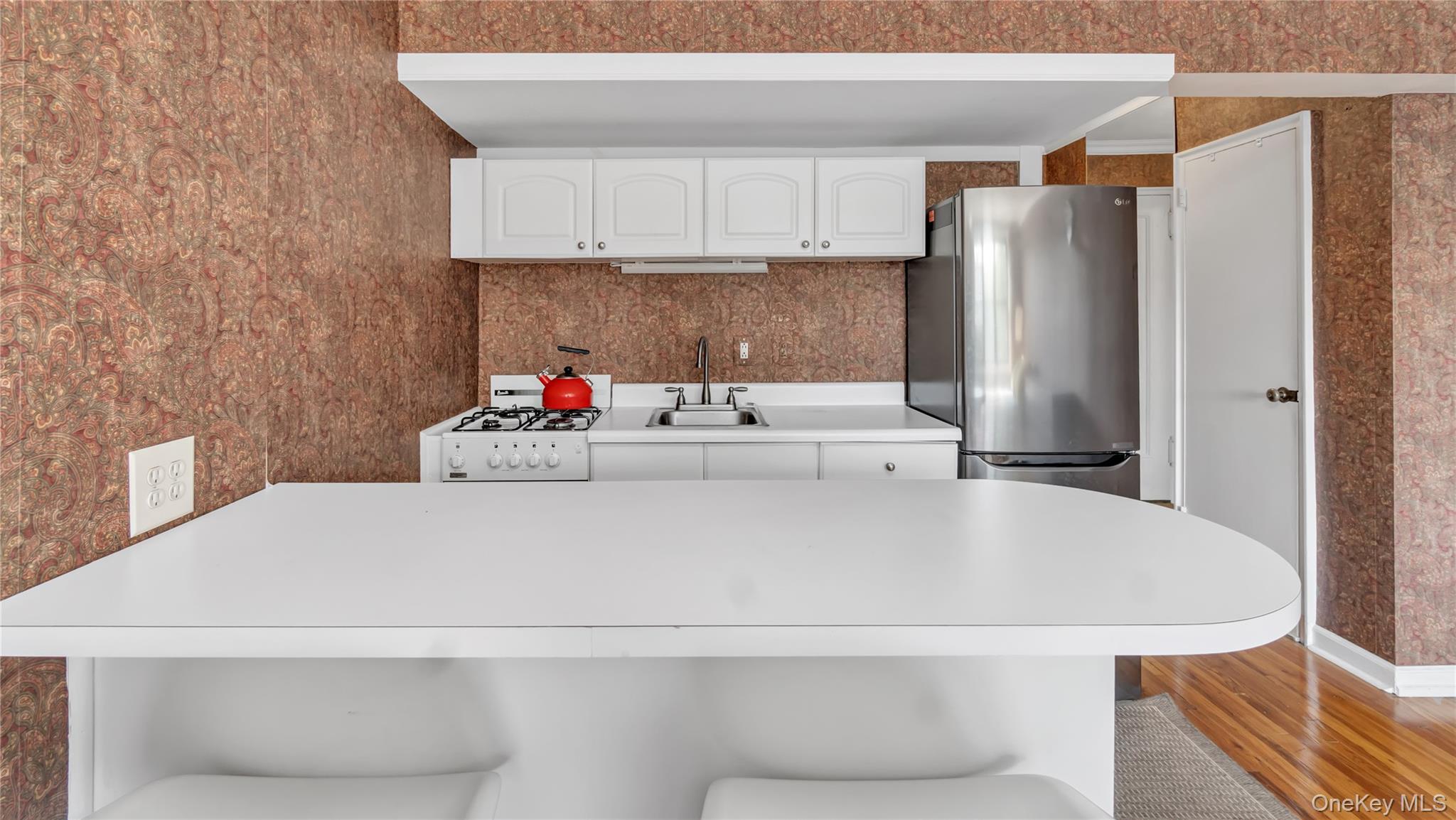 15 Canterbury Road, Unit D18 Great Neck, NY 11021 - Photo 6 of 10 Kitchen featuring white cabinets, freestanding refrigerator, wallpapered walls, a breakfast bar area, and wood finished floors