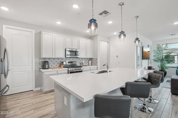 a kitchen with stainless steel appliances kitchen island granite countertop a refrigerator a stove a sink a dining table and chairs with wooden floor