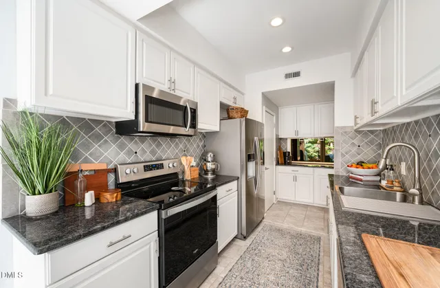 a kitchen with stainless steel appliances granite countertop a refrigerator a stove top oven a sink a counter space and cabinets