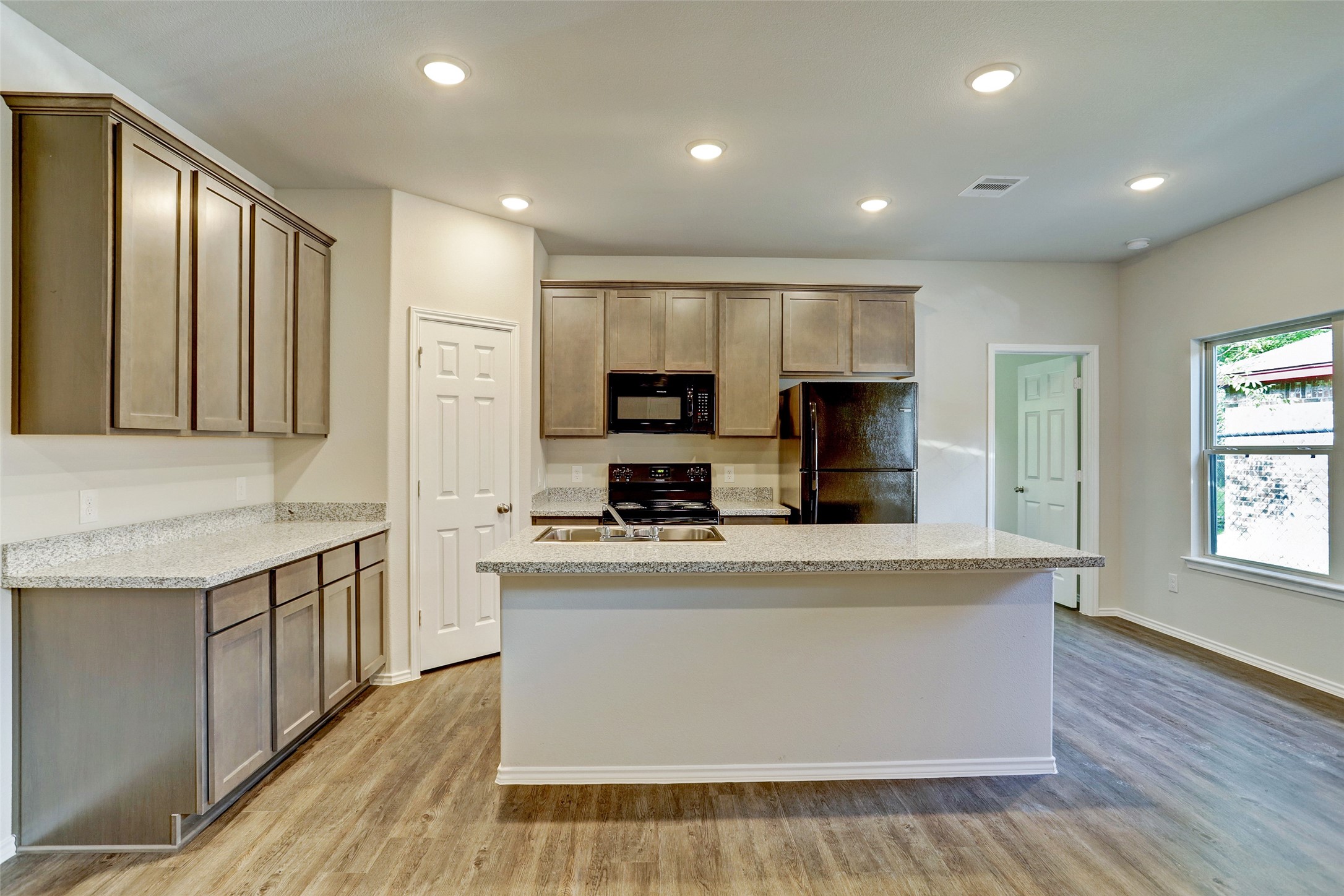 409 South 12th Street, Unit B Conroe, TX 77301 - Photo 1 of 14 Modern kitchen with granite countertops, ample cabinetry, and stainless steel appliances. Features recessed lighting, an island with a sink, and wood-style flooring. Bright and functional space with a window for natural light.