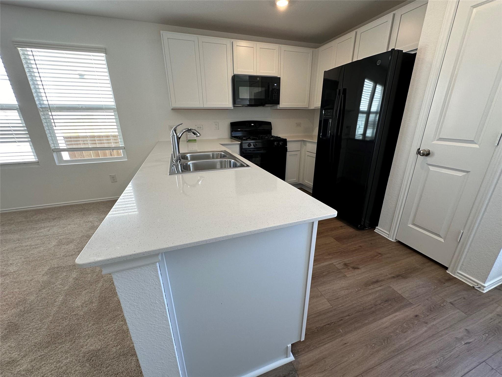 233 Magalia Lane Kyle, TX 78640 - Photo 9 of 37 Kitchen with black appliances, white cabinetry, a peninsula, and healthy amount of natural light