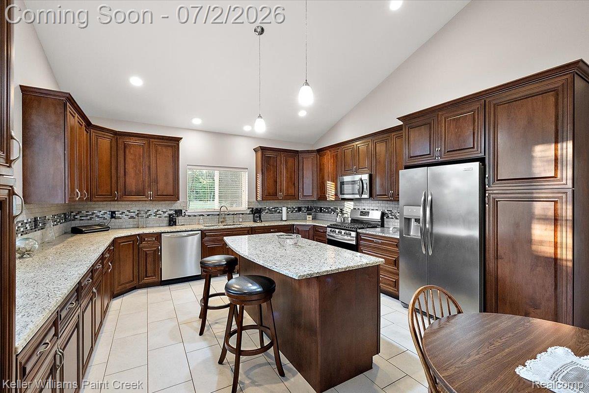 54230 Card Road Macomb, MI 48042 - Photo 36 of 73 Spacious kitchen featuring extensive dark wood cabinetry, light-toned countertops, a central island with seating, a patterned backsplash, and stainless steel appliances