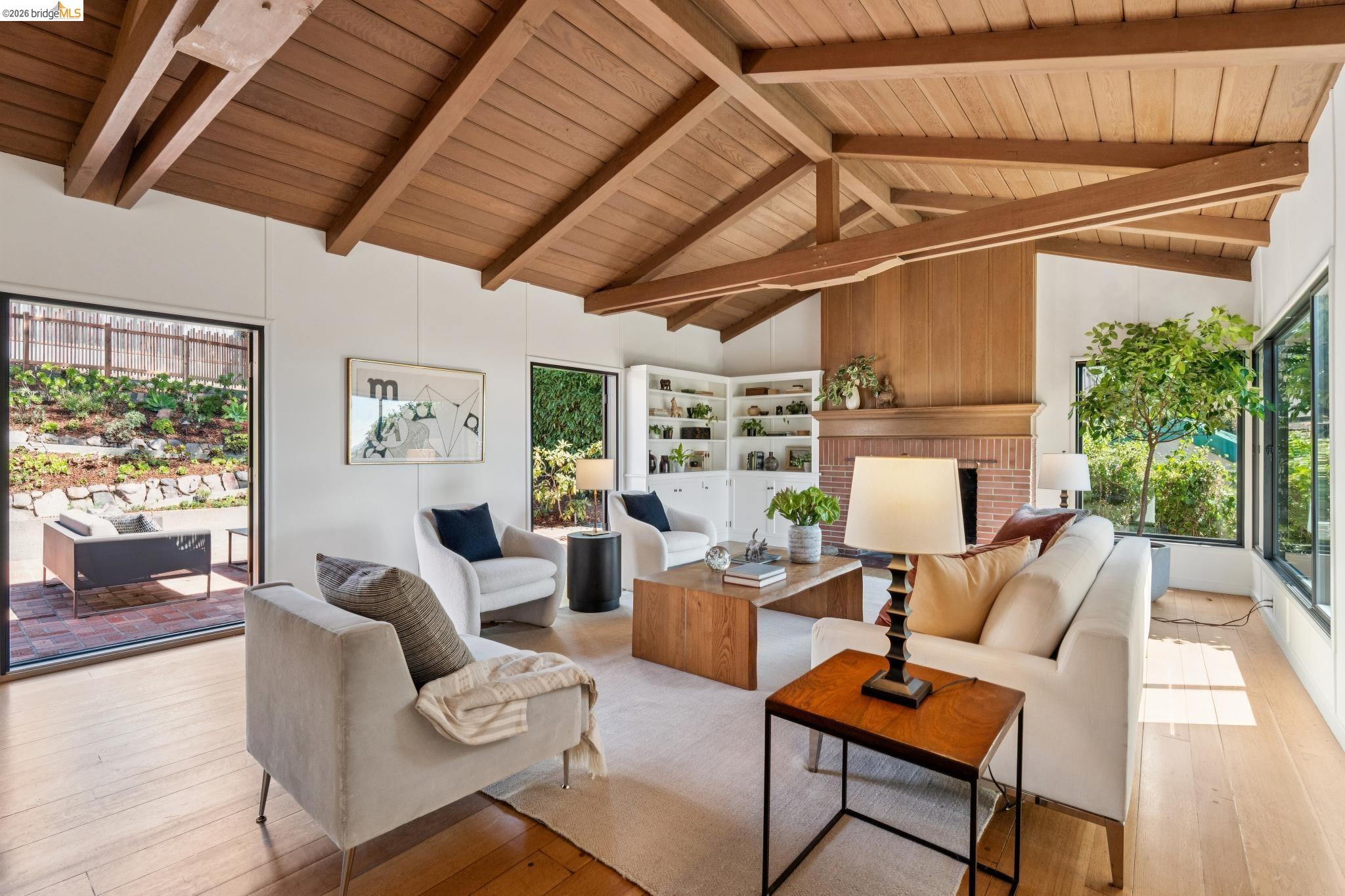 Vaulted wood-paneled ceiling with exposed beams, wood-finish flooring, brick fireplace with wood paneling, built-in shelving, and multiple large windows