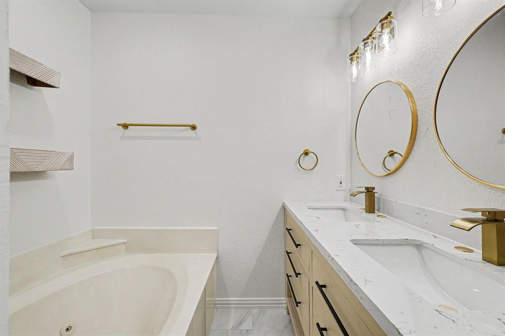 307 Dixon Street Terrell, TX 75160 - Photo 19 of 32 Bathroom featuring a built-in soaking tub with surround, a double vanity with stone-finish countertop, undermount sinks, and gold-tone fixtures
