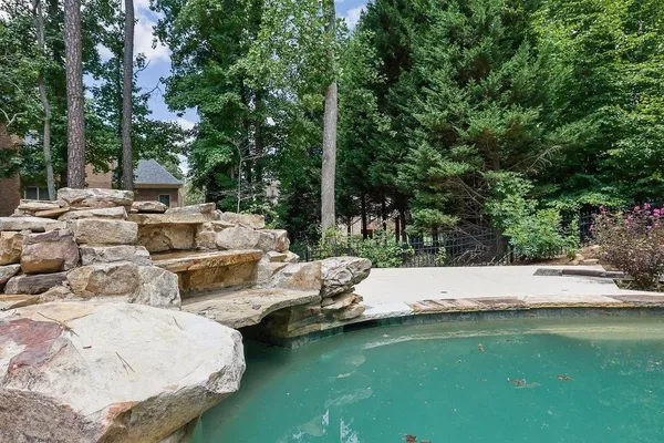 a view of swimming pool with lawn chairs and large trees